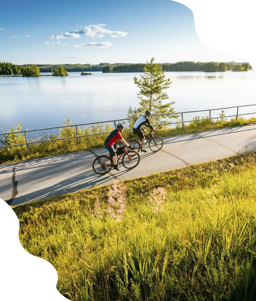 Kaksi miestä pyöräilee kauniissa maisemassa Saimaan vierellä kuökevaa pyörätietä